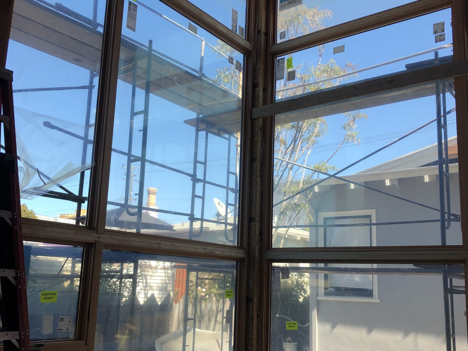 Floor-to-ceiling corner window wall newly installed in a framed opening, factory labels still on the glass
