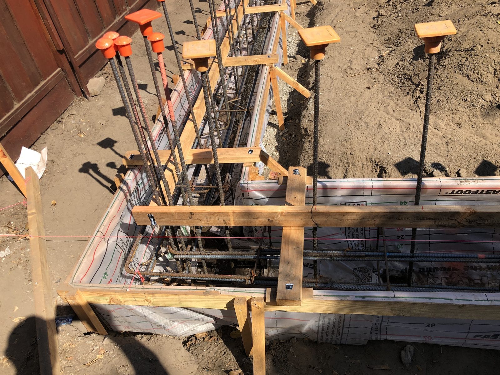 Deep footing trench with a tied rebar cage, formwork and orange safety caps on the vertical bars, ready for inspection