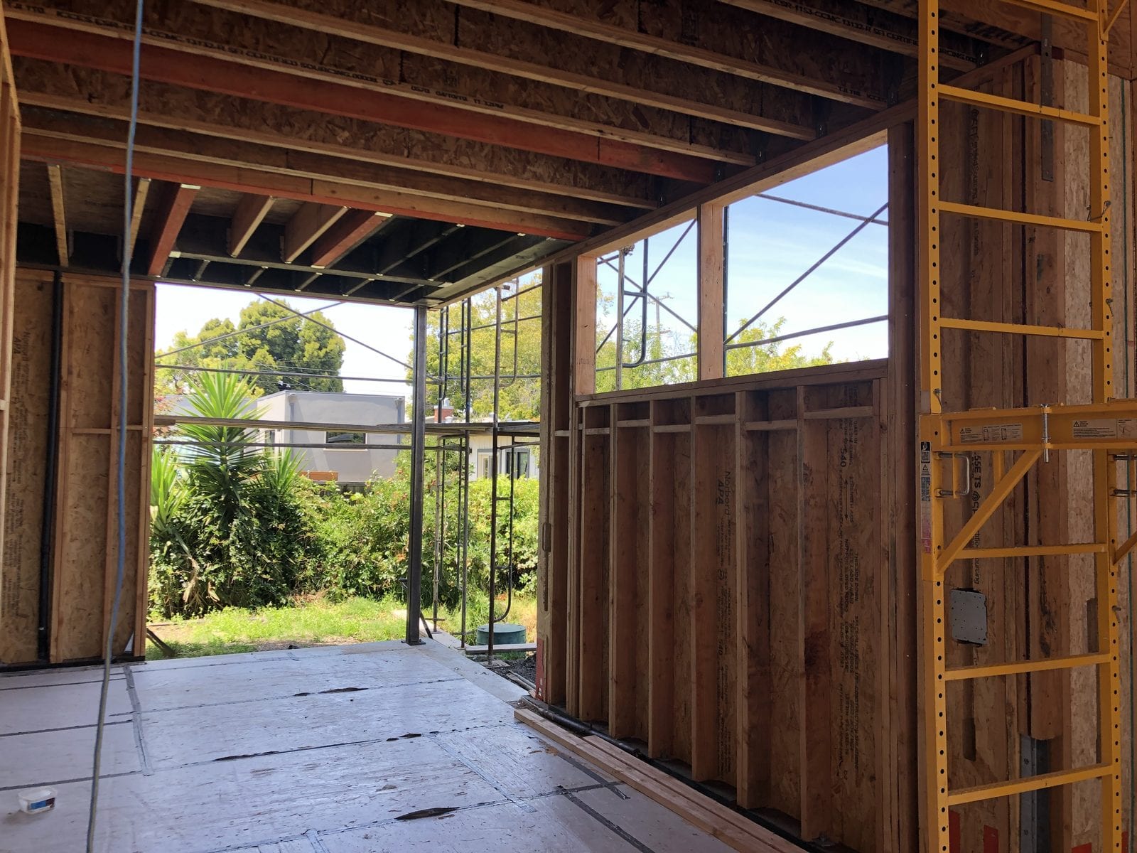 Ground-floor garage opening framed with new studs and a header, with a scaffold outside and window openings glazed