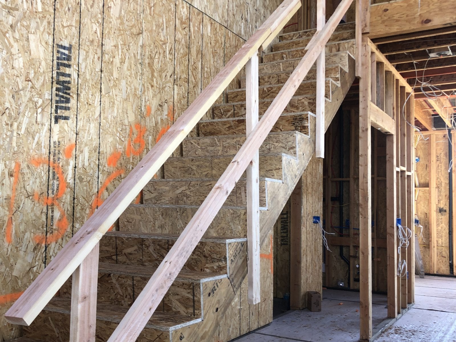 New staircase framed in place with cut stringers, a temporary handrail and OSB sheathing on the surrounding walls