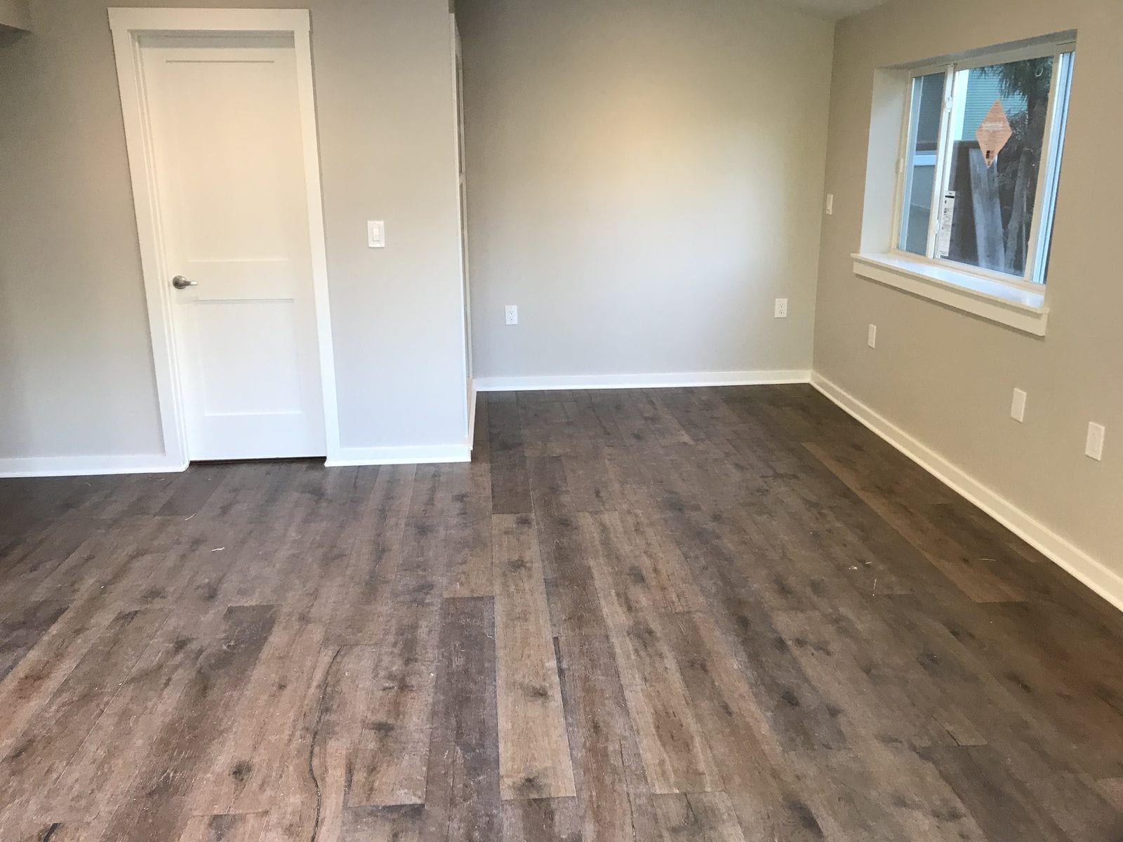 Empty room finished with wide-plank engineered wood flooring, fresh white baseboards, a new interior door and a painted window surround